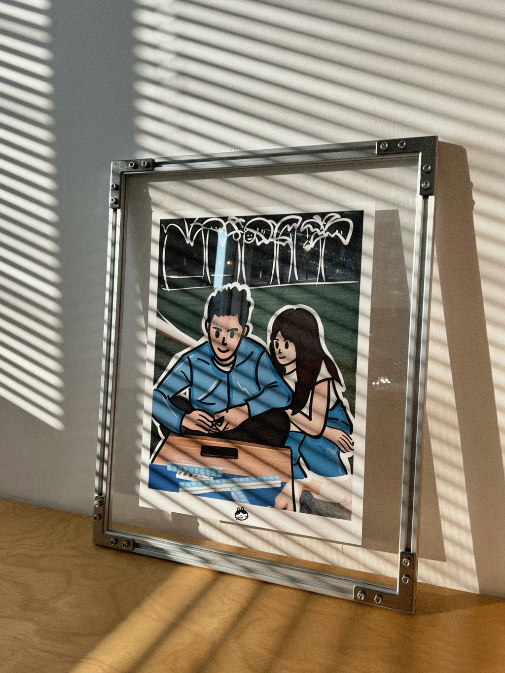 HushLume 2020 aluminum industrial picture frame with a custom couples illustration, beautifully captured under venetian blind shadows on a wooden desk.