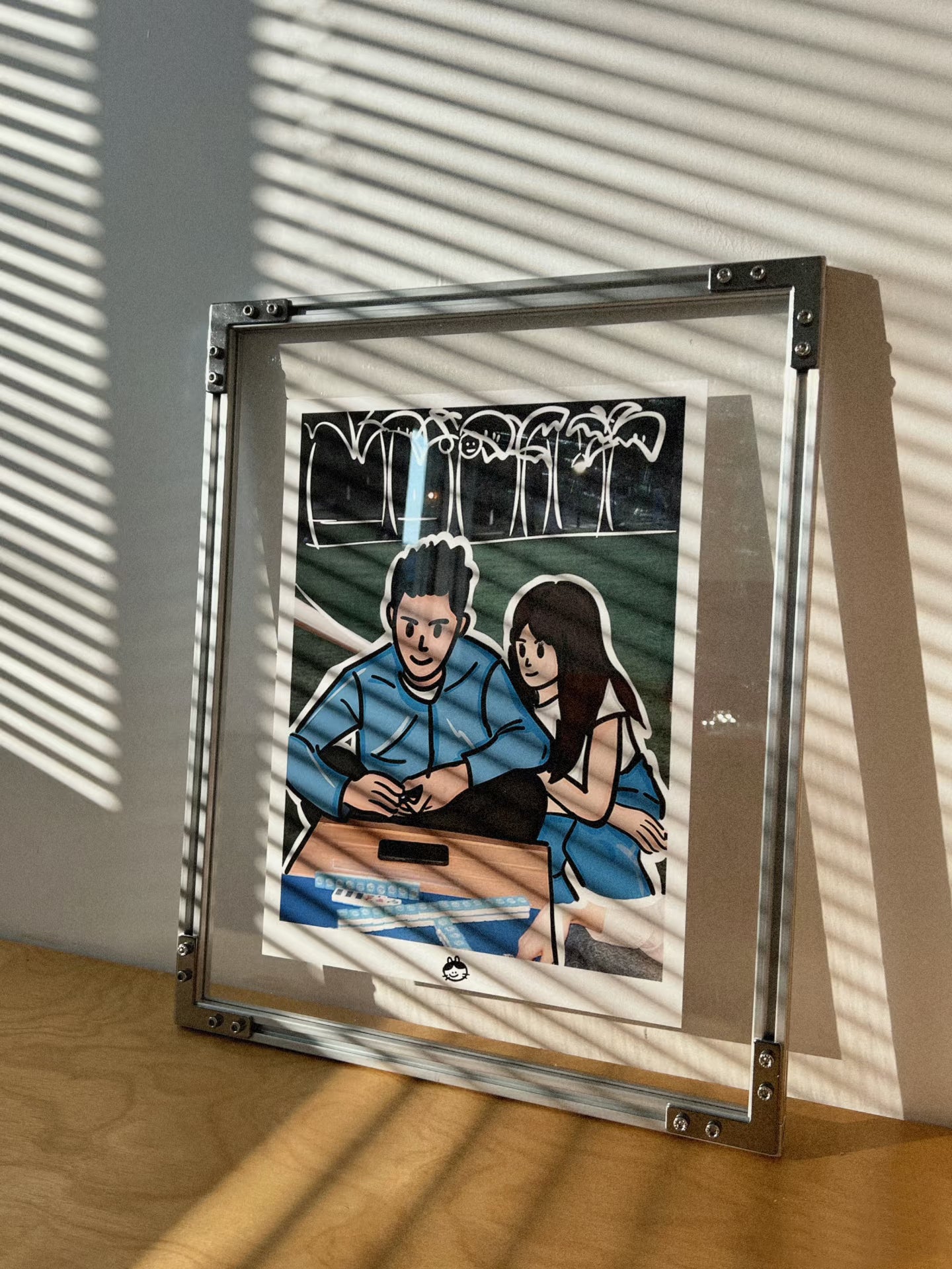 HushLume 2020 aluminum industrial picture frame with a custom couples illustration, beautifully captured under venetian blind shadows on a wooden desk.