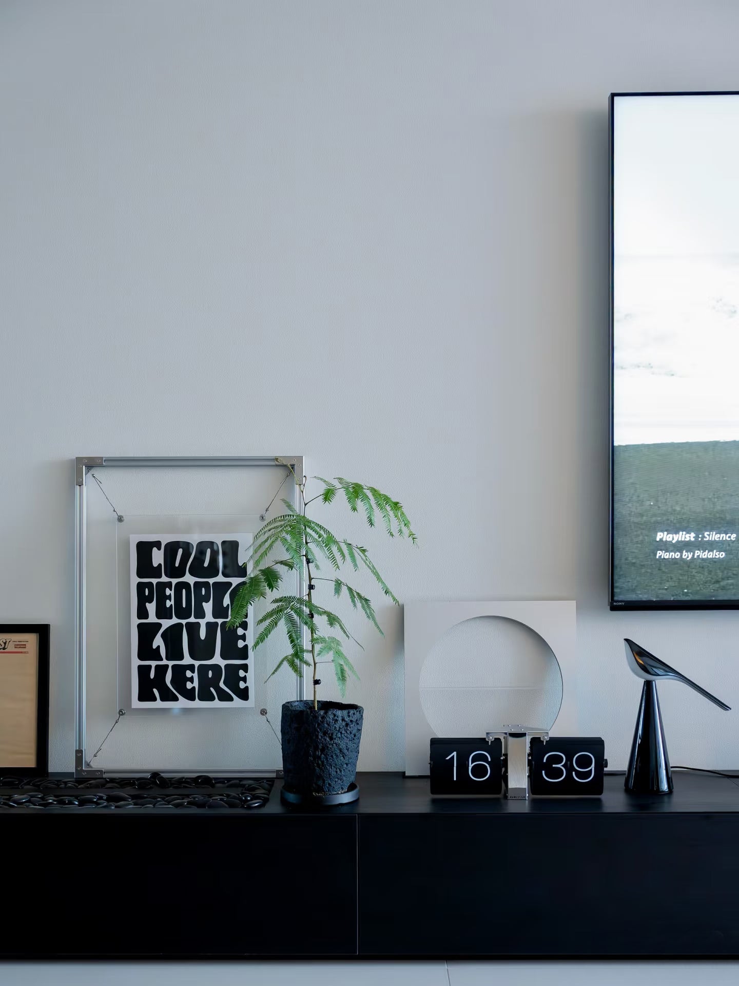 HushLume 2020 aluminum floating picture frame with steel wire suspension and dual 3mm acrylic panels, displaying a minimalist art print on a modern TV stand.