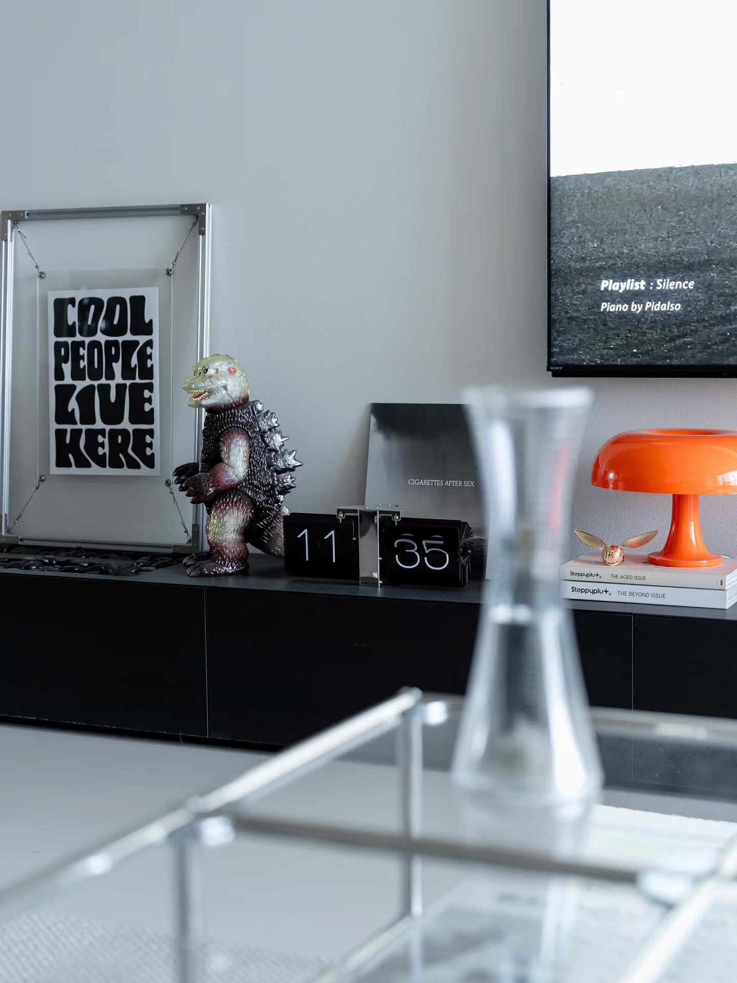 Lifestyle scene of HushLume 2020 aluminum floating frame with a trendy vinyl record, vintage kaiju toy, and a bright orange mushroom lamp on a minimalist console.