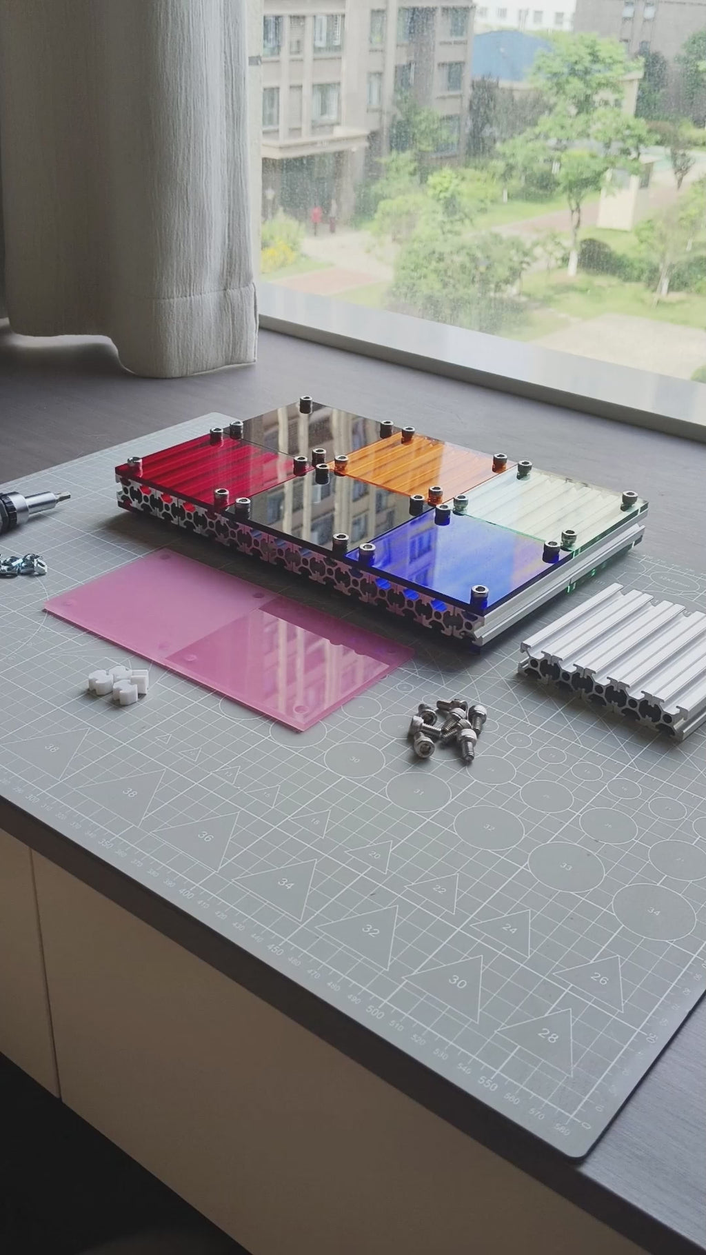 Video screenshot of a DIY assembly tutorial for the HushLume 10x10cm industrial coaster, showcasing aluminum extrusions, hex screws, and custom pink acrylic panels.