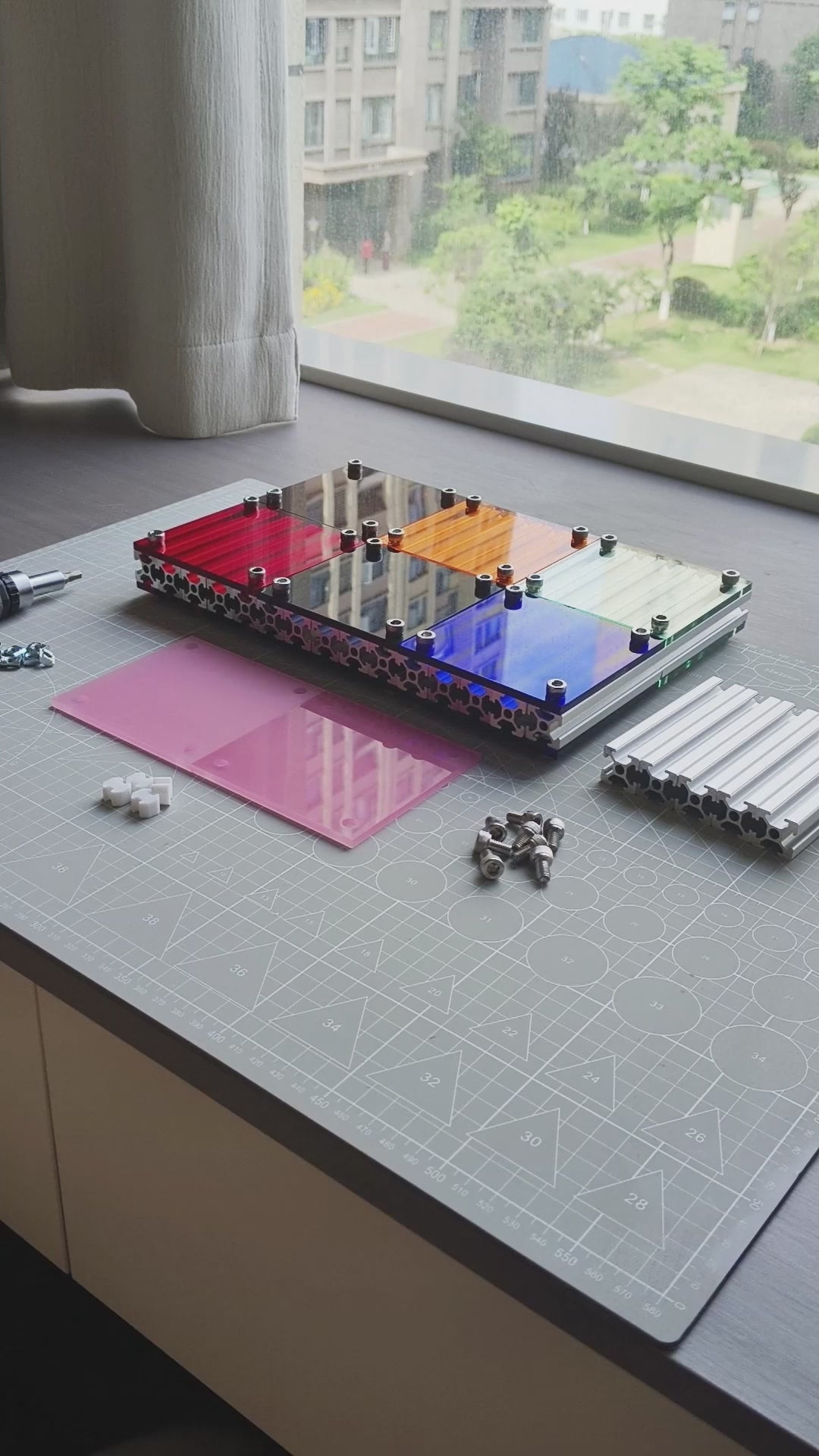 Video screenshot of a DIY assembly tutorial for the HushLume 10x10cm industrial coaster, showcasing aluminum extrusions, hex screws, and custom pink acrylic panels.
